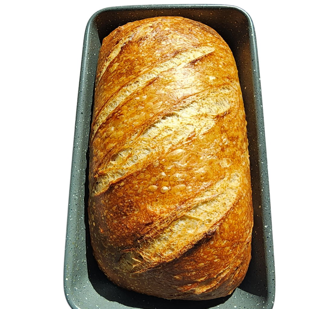 Freshly baked artisan sourdough loaf with a golden-brown crust in a metal baking pan.