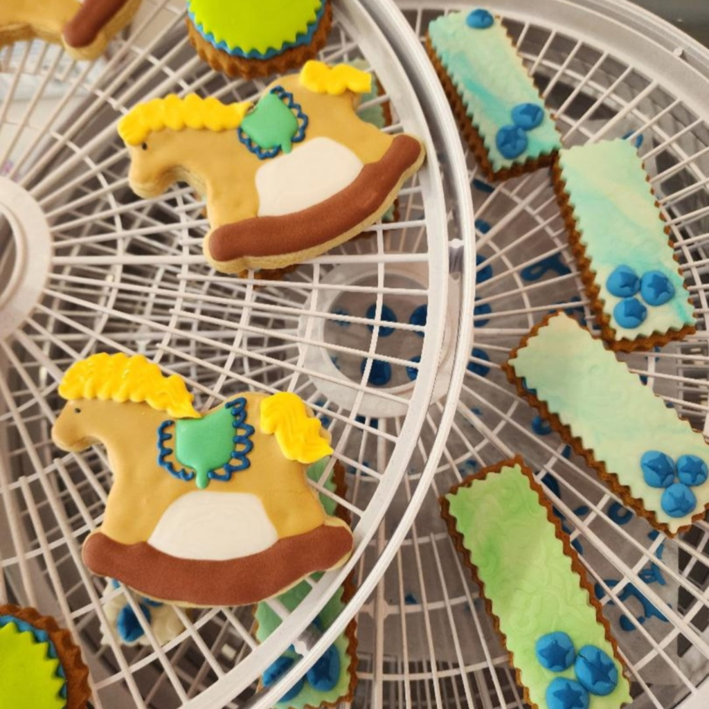 Hand-decorated rubber ducky sugar cookies with blue and yellow royal icing on a professional drying rack.