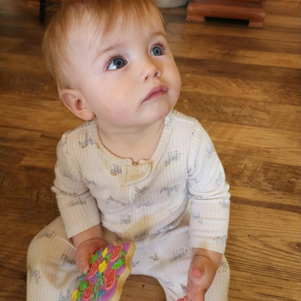 A toddler holding a colorful, star-shaped Pioneer Spirit cookie while looking up.