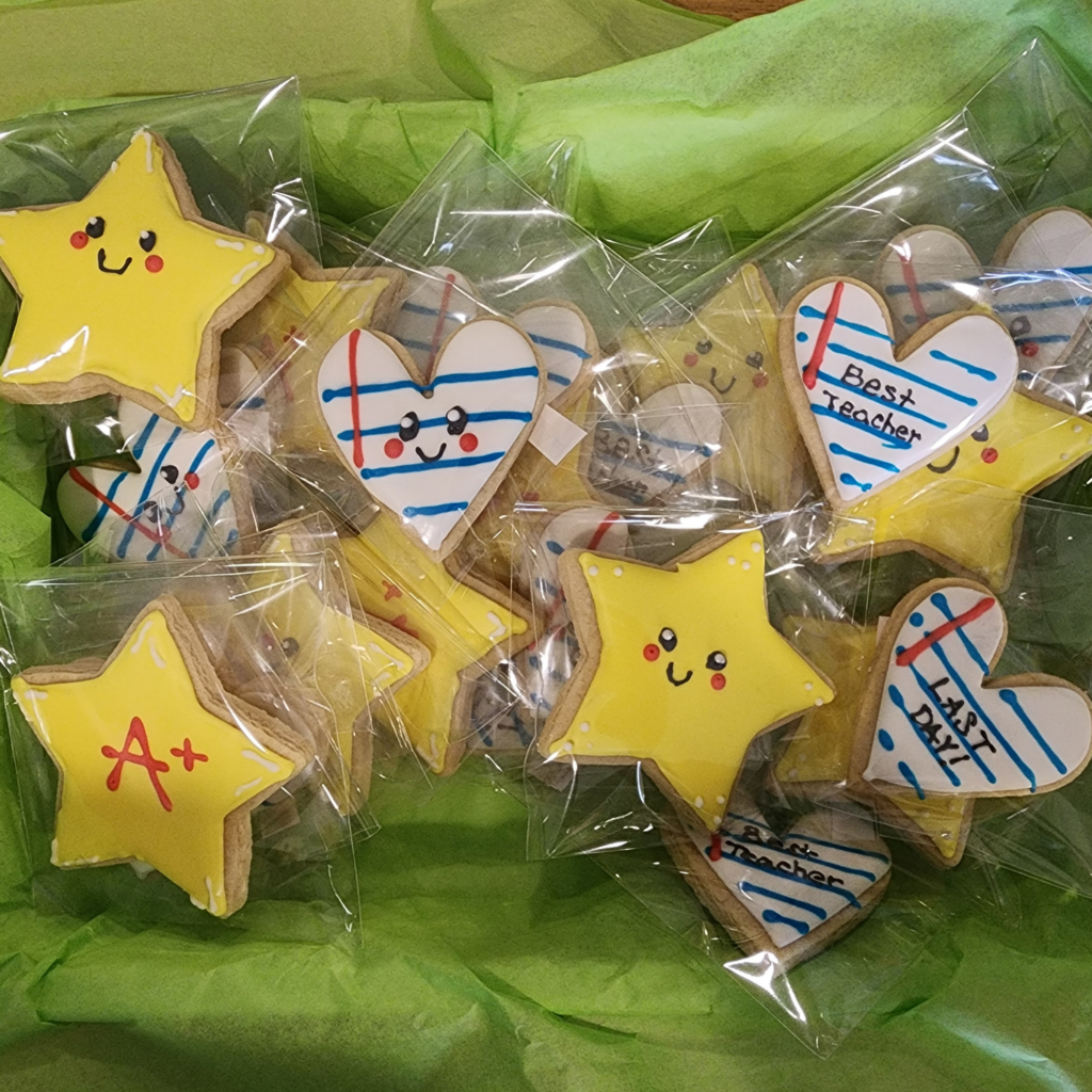 Hand-decorated school-themed sugar cookies shaped like stars and hearts, featuring 'A+' and 'Best Teacher' text.
